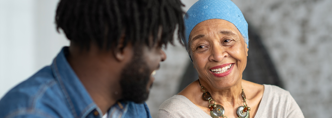 older cancer patient with head wrap smiles at companion 