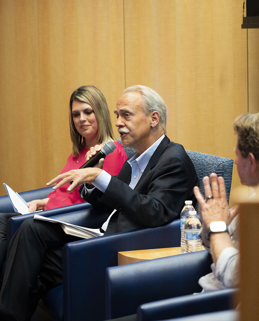 Brubaker and Wormser on stage, seated, Wormser speaking into microphone